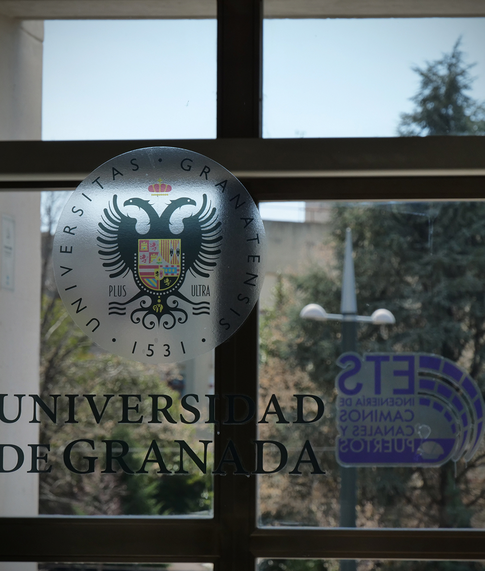 Detalle puerta edificio politécnico con vinilos del logo de la ETS. de Ingeniería en Caminos, Canales y Puertos y de la Universidad de Granada